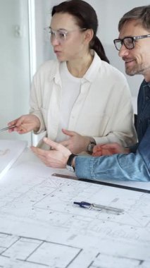 Mimarlar tasarım üzerinde işbirliği yapıyor, modern ofis ortamında planlar ve mimari modelleri tartışıyor, inşaat planlama ve mühendislik projelerinin geliştirilmesine odaklanıyor