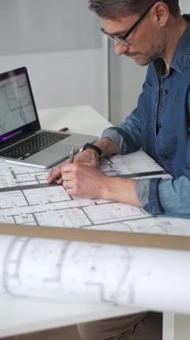 Profesyonel mimar, mimari planlarla kaplı bir masanın üzerine ayrıntılı planlar çiziyor. Hem geleneksel araçlardan hem de modern dizüstü bilgisayarlardan tasarım için yararlanmak. Planlama. Ve kentsel gelişim