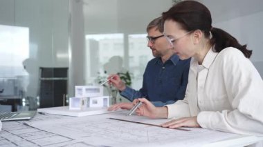 Mimarlar yeni bir yapı projesi geliştiriyor, tasarım detayları üzerinde işbirliği yapıyor ve tartışıyorlar, planlar, ölçekli bir model ve inşaatı planlamak için araçlar kullanıyorlar