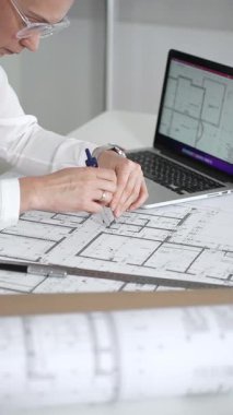 Kadın mimar, ayrıntılı bina planları üzerinde titizlikle çalışıyor. Masasına yayılmış. Mimari tasarımları parlak bir şekilde geliştirirken bir kalem ve cetvel kullanmak. Çağdaş ofis ortamı