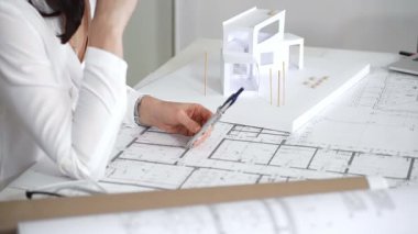 Ofiste bina planları üzerinde çalışan mimar, dizüstü bilgisayarla planlar ve kat planlarını analiz eden, yeni inşaat projeleri tasarlayan, konut ve ticari yapılar planlayan