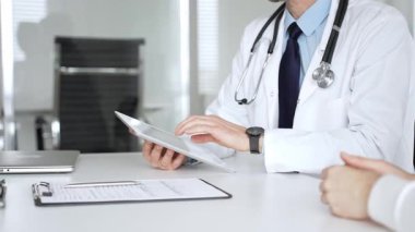 Doktorun hastaya danışması, bir klinik masasında tablet kullanması modern tıp ve dijital sağlık hizmetleri teşhisini sembolize ediyor. Tıp, sağlık ve bilim konsepti