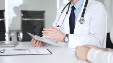 Doktorun hastaya danışması, bir klinik masasında tablet kullanması modern tıp ve dijital sağlık hizmetleri teşhisini sembolize ediyor. Tıp, sağlık ve bilim konsepti