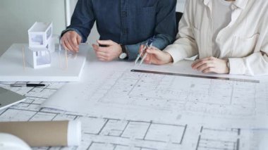 İnşaat planları üzerinde işbirliği yapan mimarlar, inşaat projesinin planlarını tartışan, ölçümler için pusula kullanan, kentsel tasarım ve mühendislik çözümleri geliştiren mimarlar
