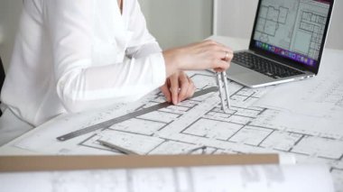 Mimarın elleri ayrıntılı planlar üzerinde ölçüm ve çizim yaparken, yeni yapılar için kavramsal tasarımlar yaratırken aynı zamanda mimari planlama sürecine yardımcı olmak için bir dizüstü bilgisayar kullanıyor.