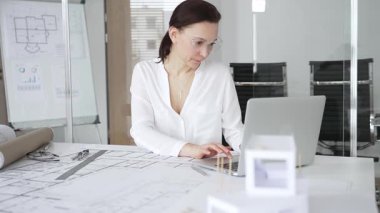 Kadın mimar, ayrıntılı bina planları üzerinde titizlikle çalışıyor. Masasına yayılmış. Mimari tasarımları parlak bir şekilde geliştirirken bir kalem ve cetvel kullanmak. Çağdaş ofis ortamı