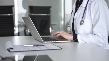 Beyaz önlüklü ve steteskoplu bir doktor dizüstü bilgisayarda daktilo kullanıyor, online sağlık kayıtlarını ve dijital tıbbi gelişmeleri yönetiyor. Tıp, sağlık ve bilim konsepti