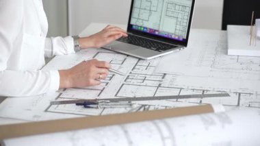 Mimarın elleri ayrıntılı planlar üzerinde ölçüm ve çizim yaparken, yeni yapılar için kavramsal tasarımlar yaratırken aynı zamanda mimari planlama sürecine yardımcı olmak için bir dizüstü bilgisayar kullanıyor.