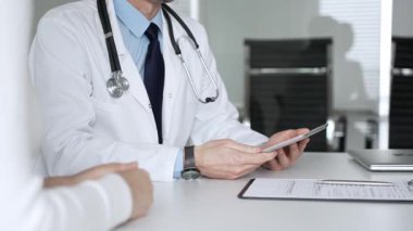 Doktorun hastaya danışması, bir klinik masasında tablet kullanması modern tıp ve dijital sağlık hizmetleri teşhisini sembolize ediyor. Tıp, sağlık ve bilim konsepti