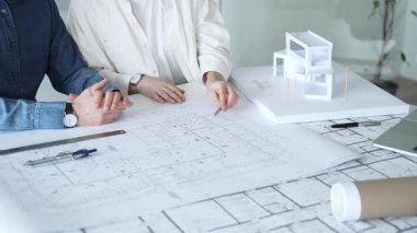 Mimarlar ve planlamacılar pusula ve dizüstü bilgisayarla ayrıntılı planları inceleyerek, bir konut projesinin kesin konut planlarını geliştirmek için bir ölçek modeli üzerinde işbirliği yapıyorlar