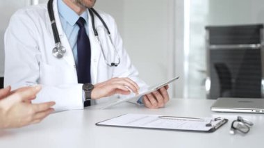 Doktorun hastaya danışması, bir klinik masasında tablet kullanması modern tıp ve dijital sağlık hizmetleri teşhisini sembolize ediyor. Tıp, sağlık ve bilim konsepti