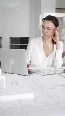 Kadın mimar, hassas ve profesyonel odaklı yenilikçi bir konut tasarımını ölçmek ve arıtmak için araçlar kullanarak, masa başında çağdaş yapı modeli ve planlarını inceler.