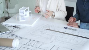 Mimarlar ve planlamacılar pusula ve dizüstü bilgisayarla ayrıntılı planları inceleyerek, bir konut projesinin kesin konut planlarını geliştirmek için bir ölçek modeli üzerinde işbirliği yapıyorlar