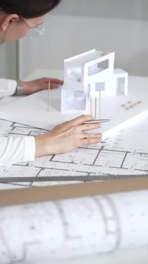 Kadın mimar, ayrıntılı bina planları üzerinde titizlikle çalışıyor. Masasına yayılmış. Mimari tasarımları parlak bir şekilde geliştirirken bir kalem ve cetvel kullanmak. Çağdaş ofis ortamı