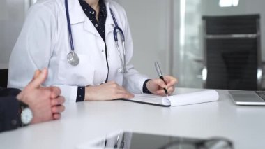 Beyaz önlüklü doktor, bir hastayla tıbbi istişare sırasında panoya notlar yazarak sağlık ve tedaviyi tartışıyor. Tıp, sağlık ve bilim konsepti