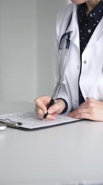 Steteskoplu beyaz önlüklü kadın doktor masadaki panoda hasta dosyasını dolduruyor klinikte tıbbi evrakları imzalıyor. Tıp, sağlık ve bilim konsepti