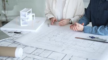 Mimarlar ve planlamacılar pusula ve dizüstü bilgisayarla ayrıntılı planları inceleyerek, bir konut projesinin kesin konut planlarını geliştirmek için bir ölçek modeli üzerinde işbirliği yapıyorlar