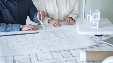 Mimarlar ve planlamacılar pusula ve dizüstü bilgisayarla ayrıntılı planları inceleyerek, bir konut projesinin kesin konut planlarını geliştirmek için bir ölçek modeli üzerinde işbirliği yapıyorlar