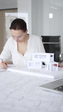 Kadın mimar, ayrıntılı bina planları üzerinde titizlikle çalışıyor. Masasına yayılmış. Mimari tasarımları parlak bir şekilde geliştirirken bir kalem ve cetvel kullanmak. Çağdaş ofis ortamı