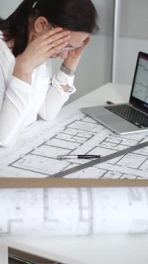 Kadın mimar, ayrıntılı bina planları üzerinde titizlikle çalışıyor. Masasına yayılmış. Mimari tasarımları parlak bir şekilde geliştirirken bir kalem ve cetvel kullanmak. Çağdaş ofis ortamı