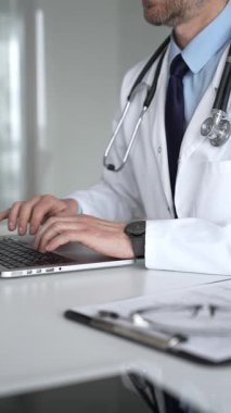 Beyaz önlüklü ve steteskoplu bir doktor gümüş bir dizüstü bilgisayarda yazı yazıyor, online tıbbi konsültasyon sağlıyor ve hasta kayıtlarını yönetiyor. Tıp, sağlık ve bilim konsepti