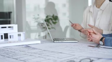 Mimarlar tasarım üzerinde işbirliği yapıyor, modern ofis ortamında planlar ve mimari modelleri tartışıyor, inşaat planlama ve mühendislik projelerinin geliştirilmesine odaklanıyor