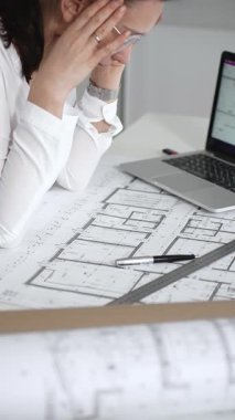 Kadın mimar, ayrıntılı bina planları üzerinde titizlikle çalışıyor. Masasına yayılmış. Mimari tasarımları parlak bir şekilde geliştirirken bir kalem ve cetvel kullanmak. Çağdaş ofis ortamı