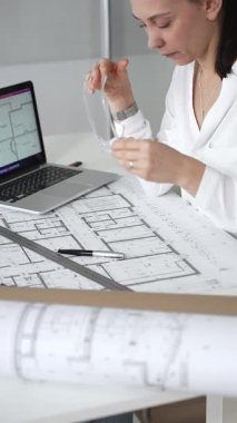 Kadın mimar, ayrıntılı bina planları üzerinde titizlikle çalışıyor. Masasına yayılmış. Mimari tasarımları parlak bir şekilde geliştirirken bir kalem ve cetvel kullanmak. Çağdaş ofis ortamı