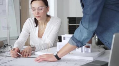 Mimarlar yeni bir bina projesi geliştiriyorlar. Meslektaşları mimari bir model, sergilenen tasarım, planlama ve takım çalışması üzerinde cetvelle çalışan bir kadın profesyonel çizim.