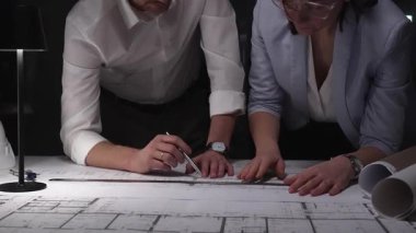 Mimarlar birlikte çalışır, bina planlarını ve planlarını analiz eder, bir ofiste tasarım kavramlarını ve mühendislik unsurlarını tartışırlar..