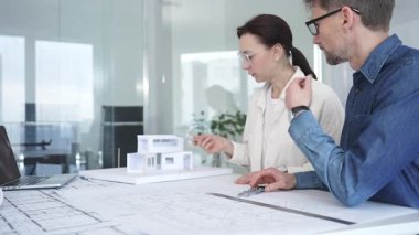 Mimarlar yeni bir yapı projesi geliştiriyor, tasarım detayları üzerinde işbirliği yapıyor ve tartışıyorlar, planlar, ölçekli bir model ve inşaatı planlamak için araçlar kullanıyorlar