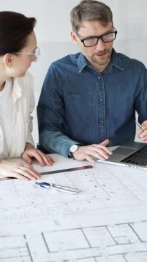 Mimarlar ve planlamacılar pusula ve dizüstü bilgisayarla ayrıntılı planları inceleyerek, bir konut projesinin kesin konut planlarını geliştirmek için bir ölçek modeli üzerinde işbirliği yapıyorlar