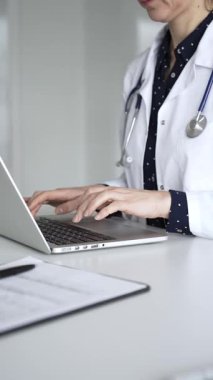 Beyaz önlüklü ve steteskoplu bir doktor dizüstü bilgisayarda daktilo kullanıyor, online sağlık kayıtlarını ve dijital tıbbi gelişmeleri yönetiyor. Tıp, sağlık ve bilim konsepti