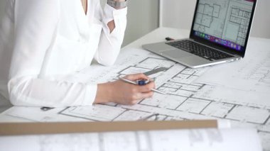 Mimarın elleri ayrıntılı planlar üzerinde ölçüm ve çizim yaparken, yeni yapılar için kavramsal tasarımlar yaratırken aynı zamanda mimari planlama sürecine yardımcı olmak için bir dizüstü bilgisayar kullanıyor.