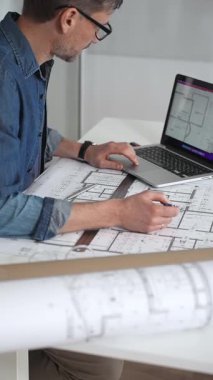 Profesyonel mimar, mimari planlarla kaplı bir masanın üzerine ayrıntılı planlar çiziyor. Hem geleneksel araçlardan hem de modern dizüstü bilgisayarlardan tasarım için yararlanmak. Planlama. Ve kentsel gelişim