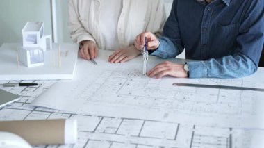 Mimarlar ve planlamacılar pusula ve dizüstü bilgisayarla ayrıntılı planları inceleyerek, bir konut projesinin kesin konut planlarını geliştirmek için bir ölçek modeli üzerinde işbirliği yapıyorlar