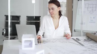 Kadın mimar, ayrıntılı bina planları üzerinde titizlikle çalışıyor. Masasına yayılmış. Mimari tasarımları parlak bir şekilde geliştirirken bir kalem ve cetvel kullanmak. Çağdaş ofis ortamı