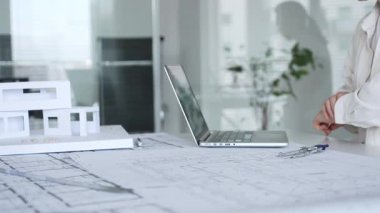 Kadın mimar, yeni bina tasarımları tasarlıyor, bir dizüstü bilgisayar ve ölçekli modelle mimari planlar üzerinde çalışıyor, kentsel planlama ve altyapı geliştirme üzerine odaklanıyor