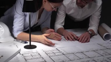 Mimarlar birlikte çalışır, bina planlarını ve planlarını analiz eder, bir ofiste tasarım kavramlarını ve mühendislik unsurlarını tartışırlar..