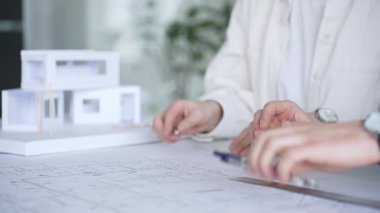 Planlar ve dizüstü bilgisayarlar üzerinde işbirliği yapan mimarlar, teknik çizimlere işaret ediyor ve bir bina projesi için çağdaş bir ofis toplantısında yapısal planlar ve tasarım ayrıntılarını tartışıyor