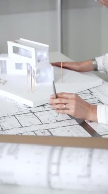 Kadın mimar, ayrıntılı bina planları üzerinde titizlikle çalışıyor. Masasına yayılmış. Mimari tasarımları parlak bir şekilde geliştirirken bir kalem ve cetvel kullanmak. Çağdaş ofis ortamı