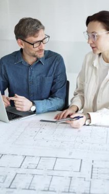 Mimarlar ve planlamacılar pusula ve dizüstü bilgisayarla ayrıntılı planları inceleyerek, bir konut projesinin kesin konut planlarını geliştirmek için bir ölçek modeli üzerinde işbirliği yapıyorlar