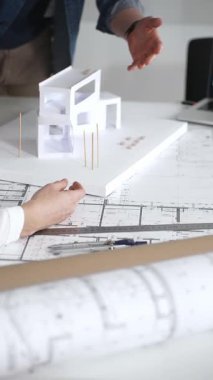 Mimarlar, tasarım ayrıntıları üzerinde işbirliği yaparak ve inşaat için yeni bir konut inşaatı projesi planlayarak, temiz bir masadaki planları ve ölçekli bir modeli inceleyecekler.