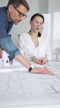 Mimarlar yeni bir bina projesi geliştiriyorlar. Meslektaşları mimari bir model, sergilenen tasarım, planlama ve takım çalışması üzerinde cetvelle çalışan bir kadın profesyonel çizim.