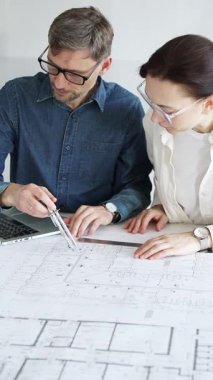 Mimarlar ve planlamacılar pusula ve dizüstü bilgisayarla ayrıntılı planları inceleyerek, bir konut projesinin kesin konut planlarını geliştirmek için bir ölçek modeli üzerinde işbirliği yapıyorlar