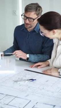 Mimarlar ve planlamacılar pusula ve dizüstü bilgisayarla ayrıntılı planları inceleyerek, bir konut projesinin kesin konut planlarını geliştirmek için bir ölçek modeli üzerinde işbirliği yapıyorlar