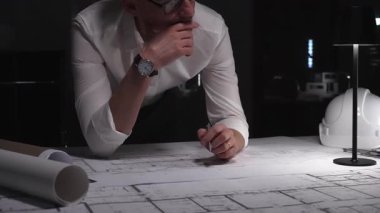 Mimarın inşaat planları üzerinde yoğunlaşması, detayları işaretlemek için bir kalem kullanması, karmaşık bina planları tasarlaması ve düşünmesi. İş ve mimarlık kavramı