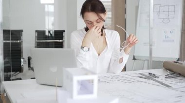 Masasında mimari planlar ve modeller üzerinde çalışan düşünceli bir kadın mimar elinde bir kalem tutuyor ve modern ofis ortamında proje detaylarını değerlendiriyor, kentsel gelişime odaklanıyor.