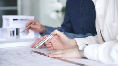 Planlar ve dizüstü bilgisayarlar üzerinde işbirliği yapan mimarlar, teknik çizimlere işaret ediyor ve bir bina projesi için çağdaş bir ofis toplantısında yapısal planlar ve tasarım ayrıntılarını tartışıyor