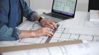 Profesyonel mimar, mimari planlarla kaplı bir masanın üzerine ayrıntılı planlar çiziyor. Hem geleneksel araçlardan hem de modern dizüstü bilgisayarlardan tasarım için yararlanmak. Planlama. Ve kentsel gelişim